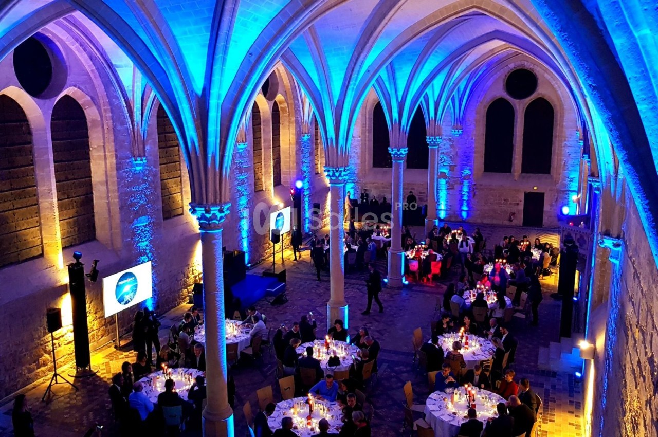 Salle voûtée éclairée en bleu accueillant un dîner avec des tables rondes dressées et des convives assis.