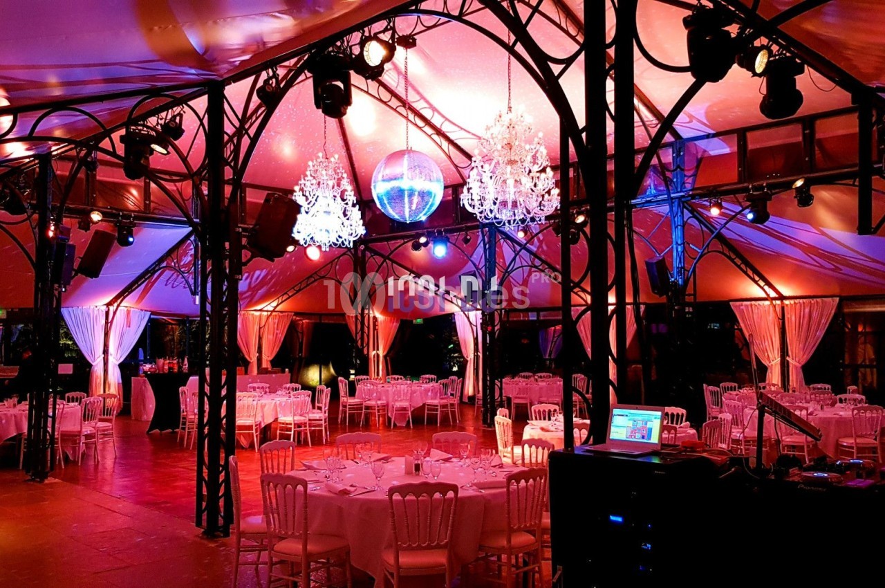 Salle de réception décorée avec des lustres, une boule disco et des tables dressées sous une lumière tamisée.