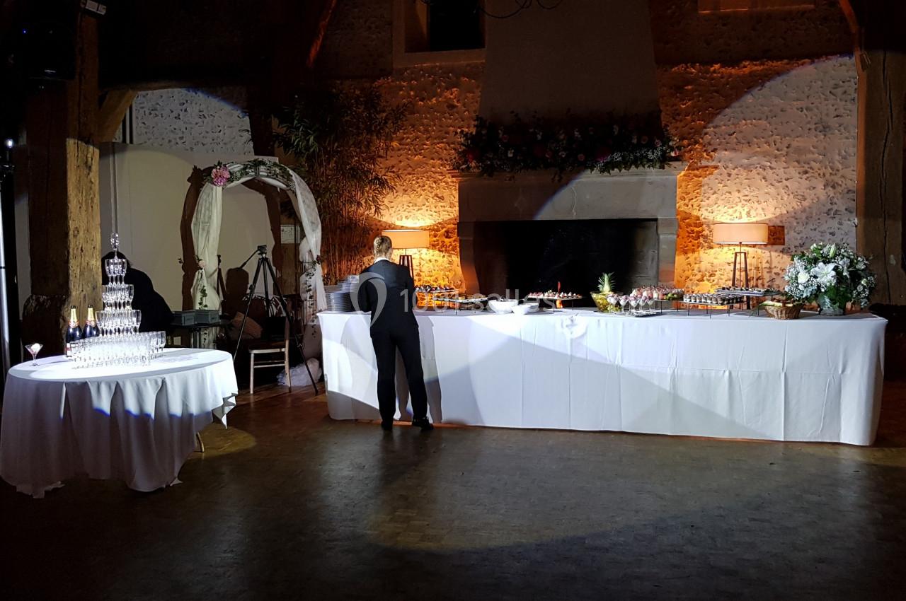 Salle de réception décorée avec une table de buffet éclairée, un présentoir à verres et une arche fleurie.