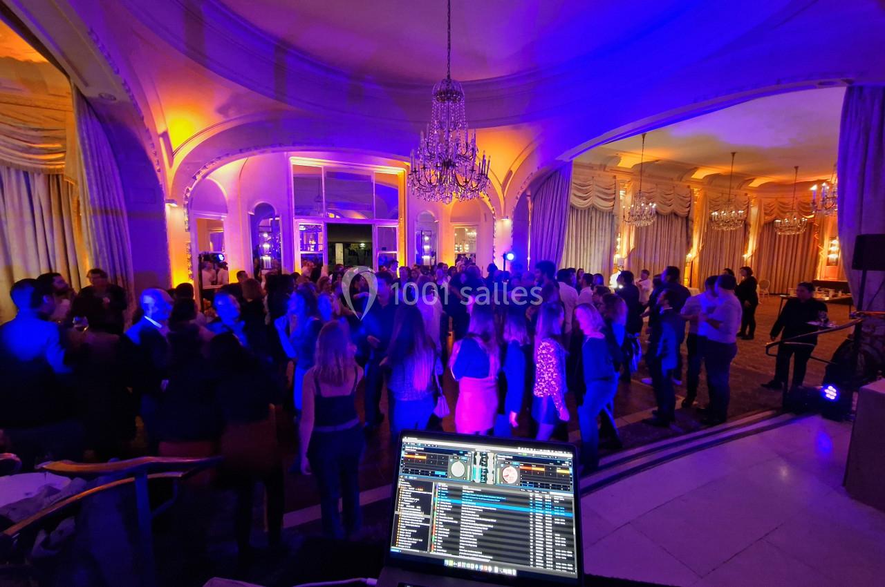Salle de réception illuminée avec des invités dansant sous des lustres, vue depuis une table de mixage de DJ.