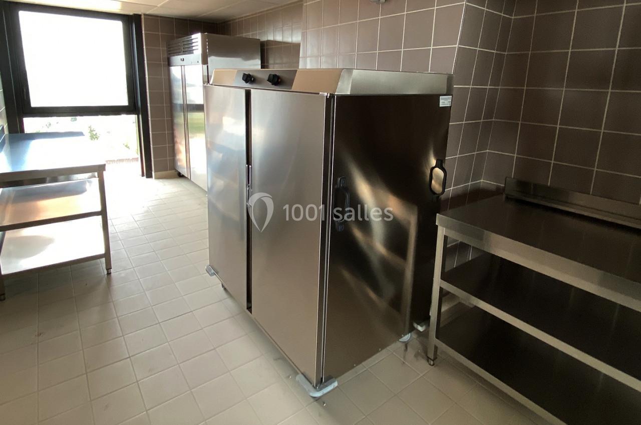 Cuisine professionnelle avec équipements en inox, incluant un réfrigérateur, des étagères et un plan de travail.