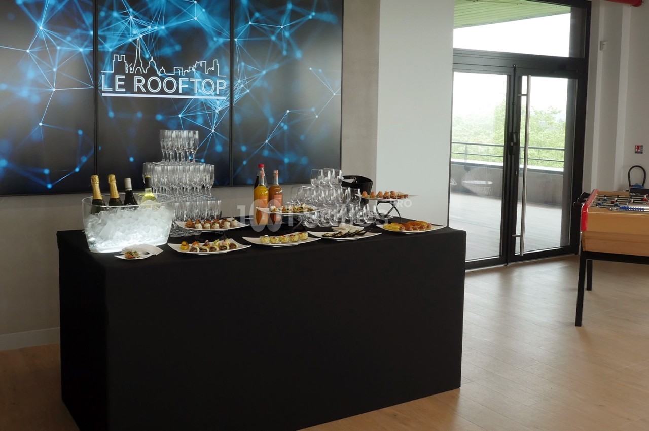 Table de réception avec boissons, verres, amuse-bouches et baby-foot en arrière-plan dans une salle lumineuse.
