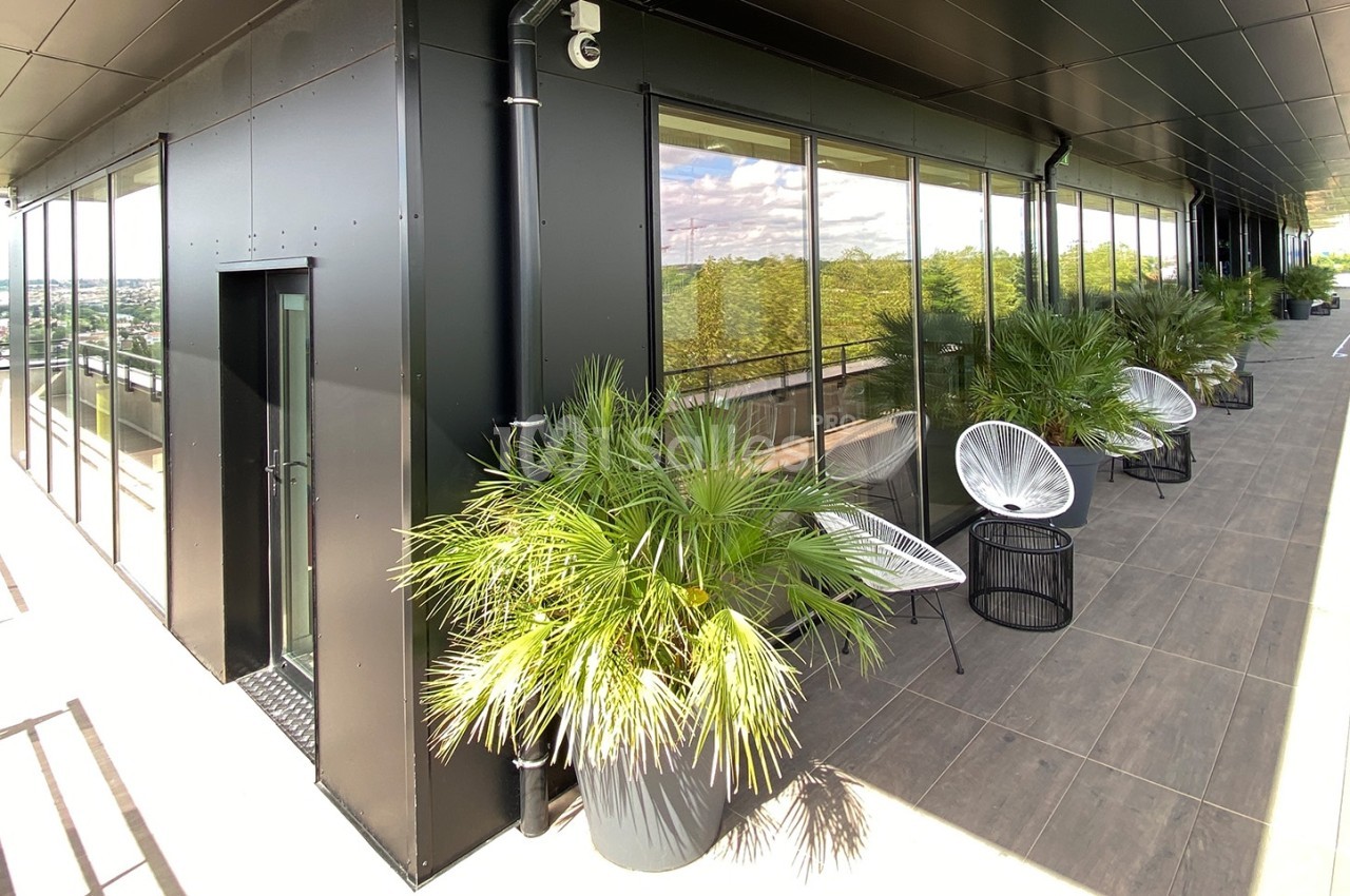 Terrasse moderne avec mobilier d'extérieur, plantes en pot et vue dégagée sur un paysage urbain et verdoyant.