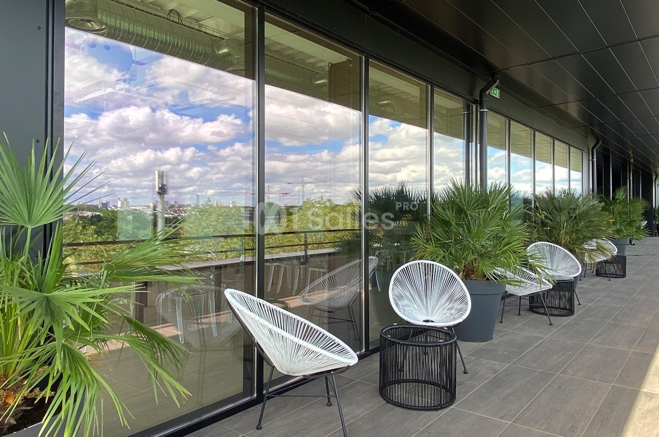 Terrasse moderne avec fauteuils design, tables basses et plantes, offrant une vue dégagée sur un paysage urbain.