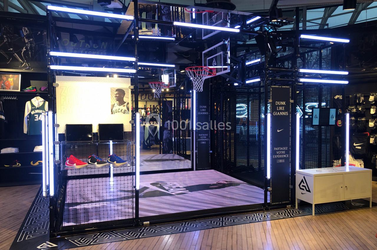 Terrain de basketball intérieur avec éclairage néon, paniers et décorations promotionnelles dans un espace commercial.