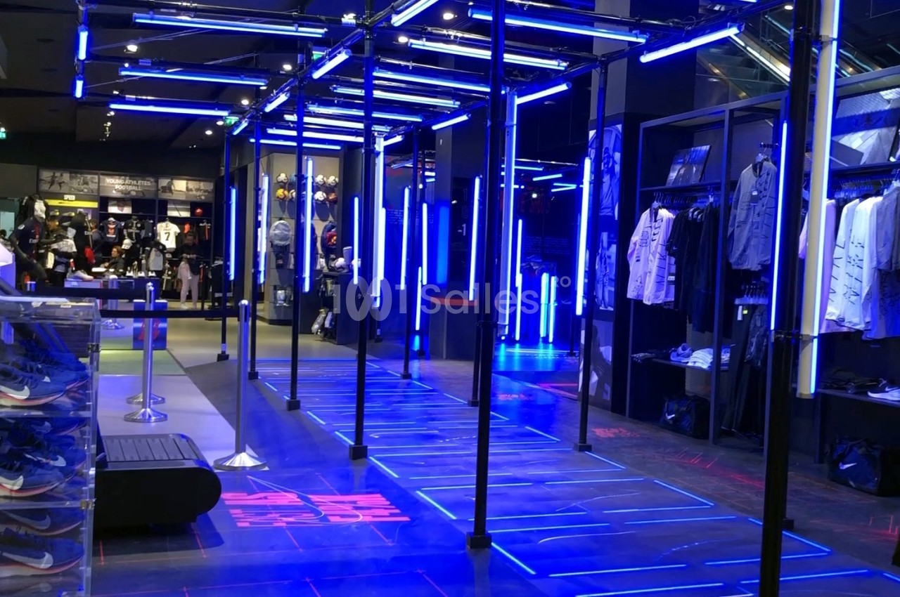 Intérieur d'un magasin moderne avec éclairage LED bleu, vêtements exposés et chaussures en vitrine.