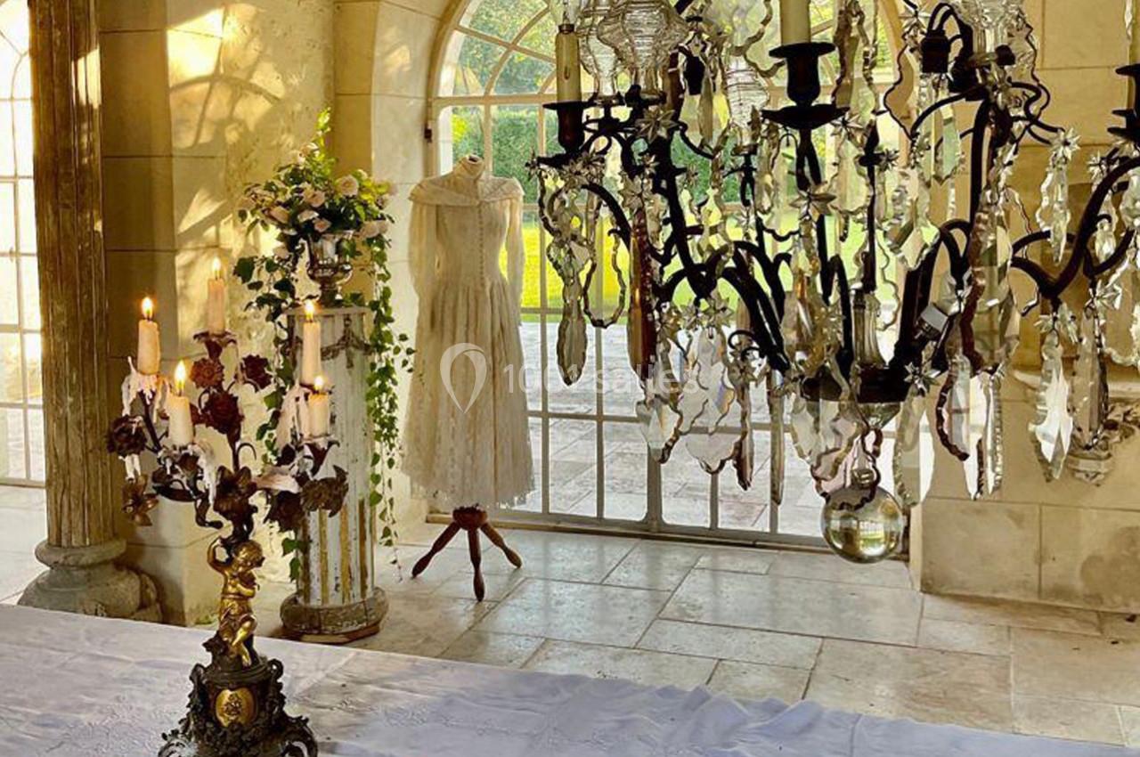Robe blanche sur un mannequin près d'une fenêtre, entourée de chandeliers et de décorations florales dans une salle…