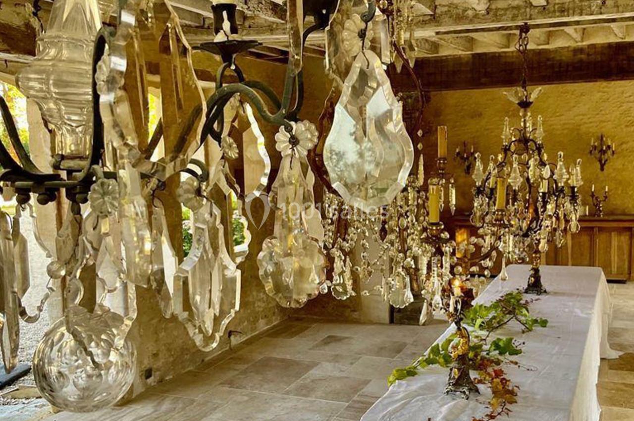 Des lustres en cristal suspendus au plafond en bois, au-dessus d'une longue table décorée de feuillages.
