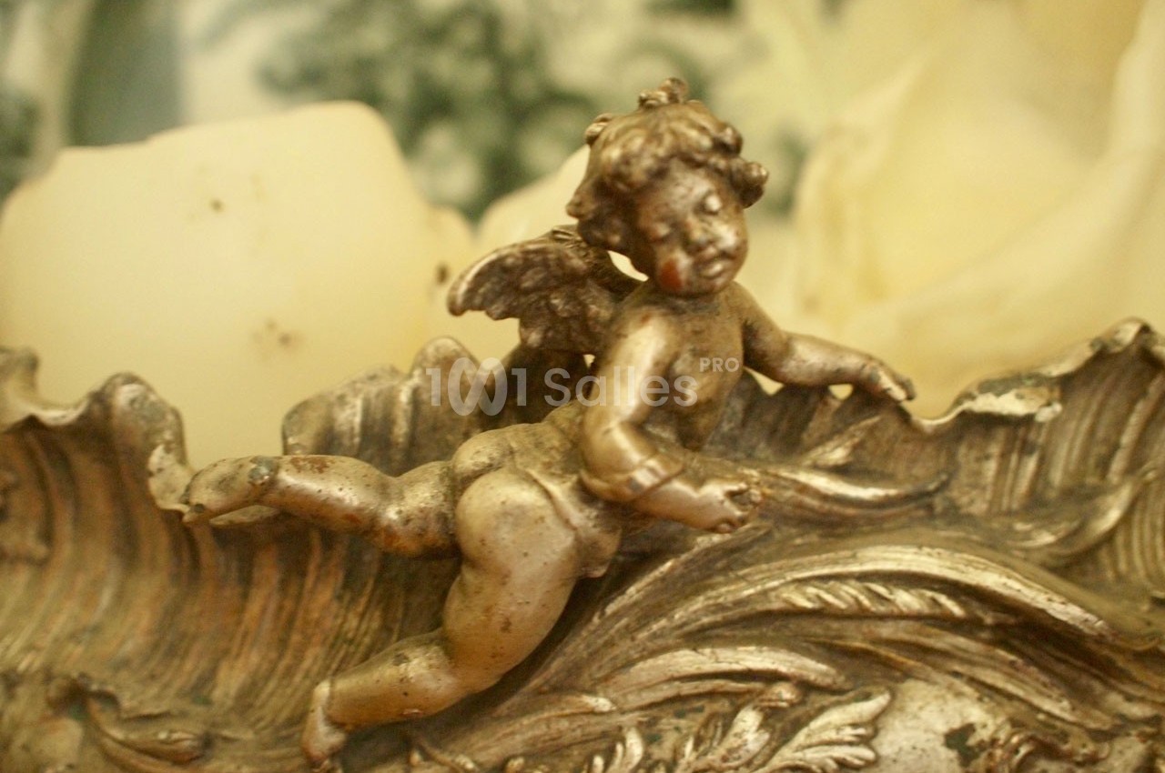 Statue en métal représentant un ange ailé allongé sur un décor ornemental aux détails sculptés.