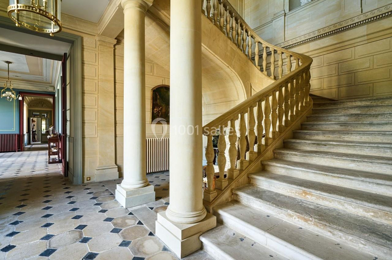 Château des Deux Lions - Escalier accès 1er étage (sans ascenseur) Escalier en pierre avec balustrade sculptée dans un intérieur lumineux aux murs clairs et sol en carreaux.