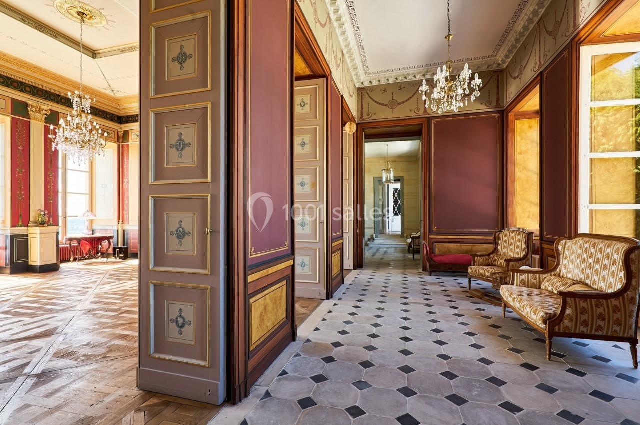 Château des Deux Lions - Hall 1er étage Intérieur d'un bâtiment ancien avec parquet, murs ornés, lustres et mobilier classique.