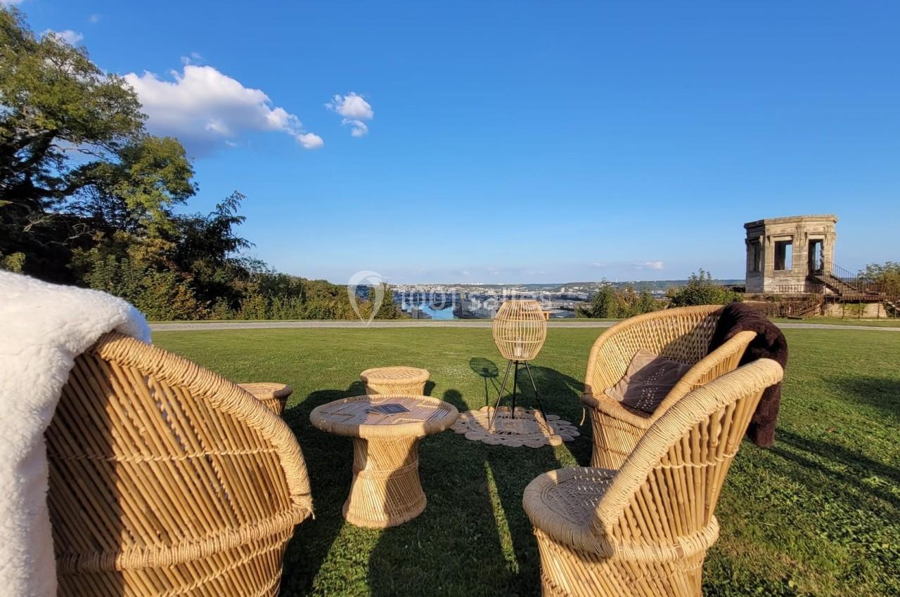 Château des Deux Lions - Vue sur Rouen Chaises et table en rotin disposées sur une pelouse avec vue sur un fleuve et un bâtiment ancien à l'arrière-plan.