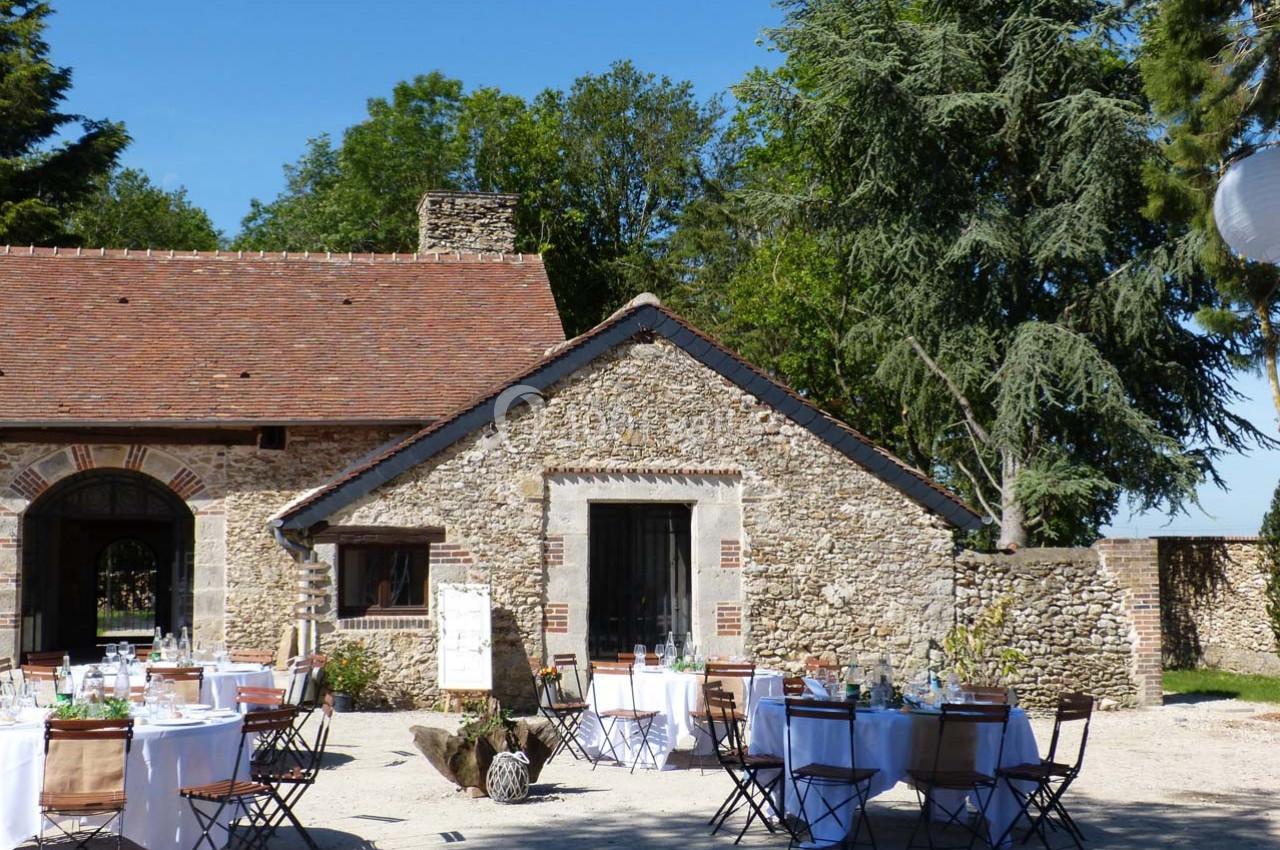 Cour extérieure avec tables dressées pour un événement devant un bâtiment en pierre sous un ciel dégagé.