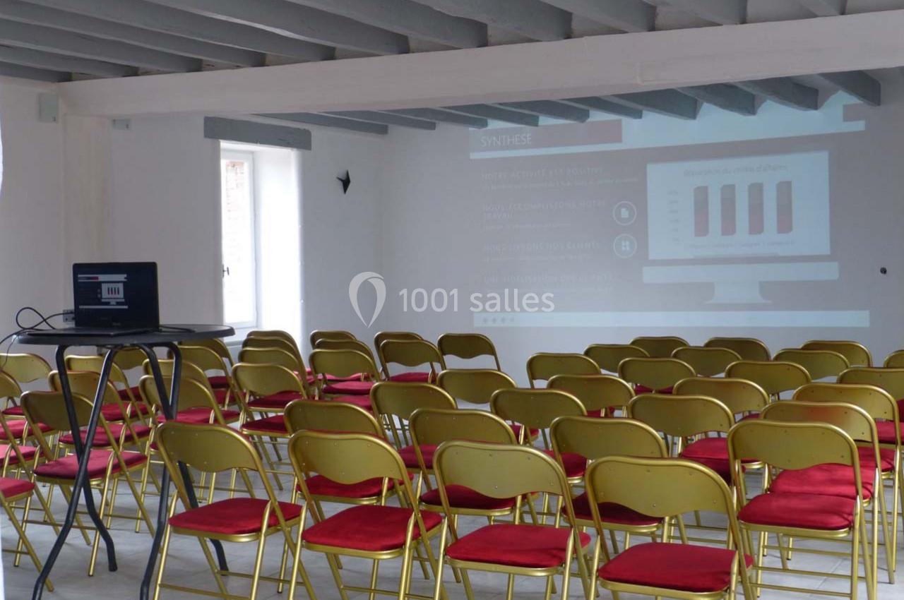 Salle de conférence vide avec des chaises jaunes et rouges, un projecteur affichant une présentation sur un écran blanc.