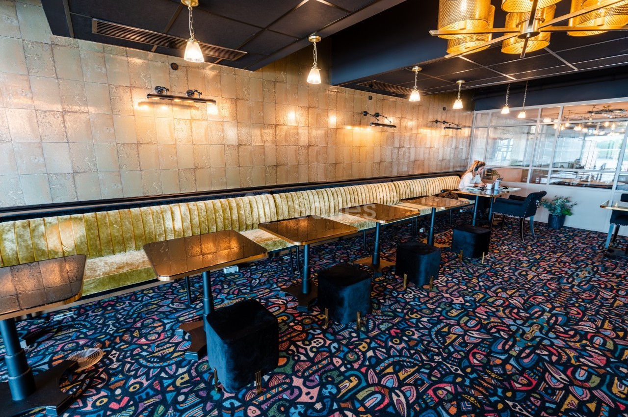 Salle de restaurant moderne avec banquette dorée, tables noires, tabourets et éclairage suspendu chaleureux.