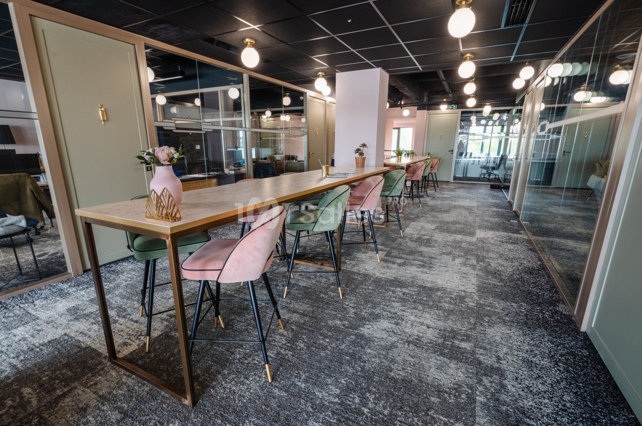 Salle de coworking moderne avec une longue table, chaises colorées, éclairage suspendu et cloisons vitrées.