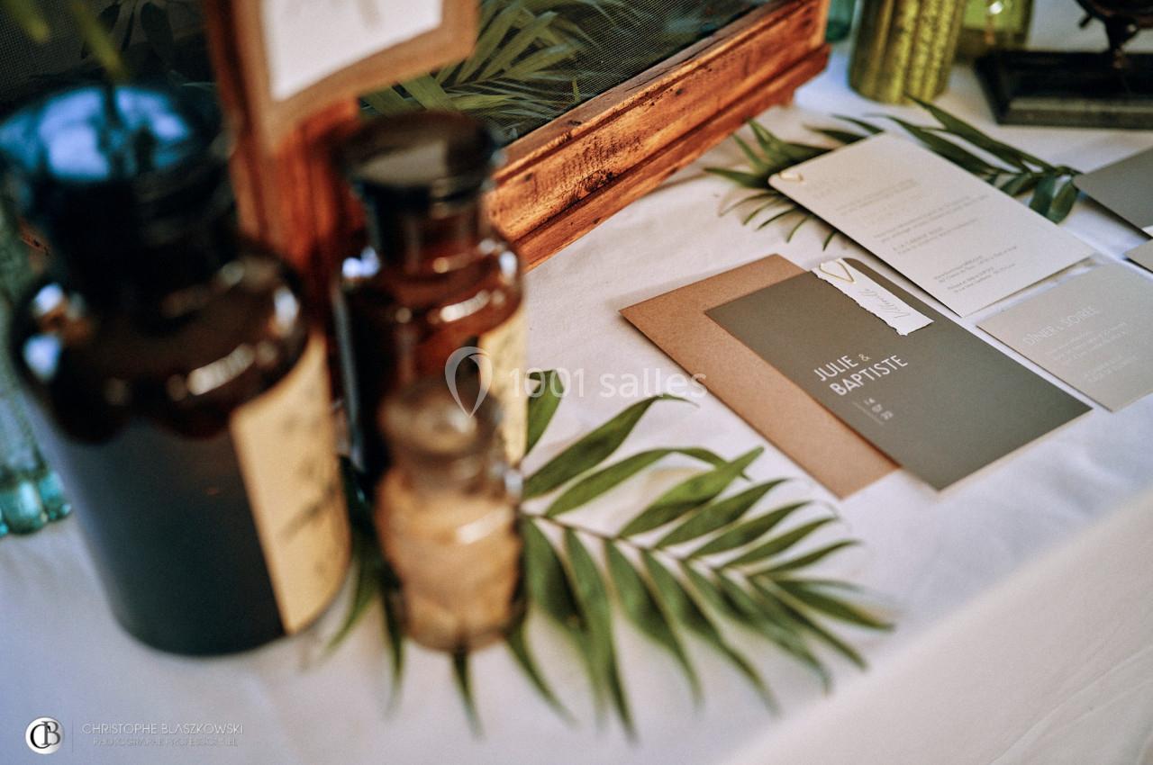 Flacons en verre, feuilles de palmier et cartes de visite disposés sur une table blanche.