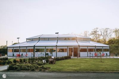 Salle de réception éclairée la nuit, avec des tables dressées visibles à travers les baies vitrées.