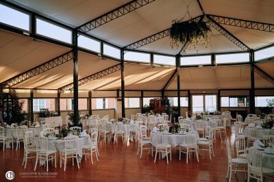 Salle de réception éclairée la nuit, avec des tables dressées visibles à travers les baies vitrées.