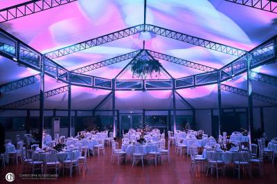 Salle de réception éclairée la nuit, avec des tables dressées visibles à travers les baies vitrées.