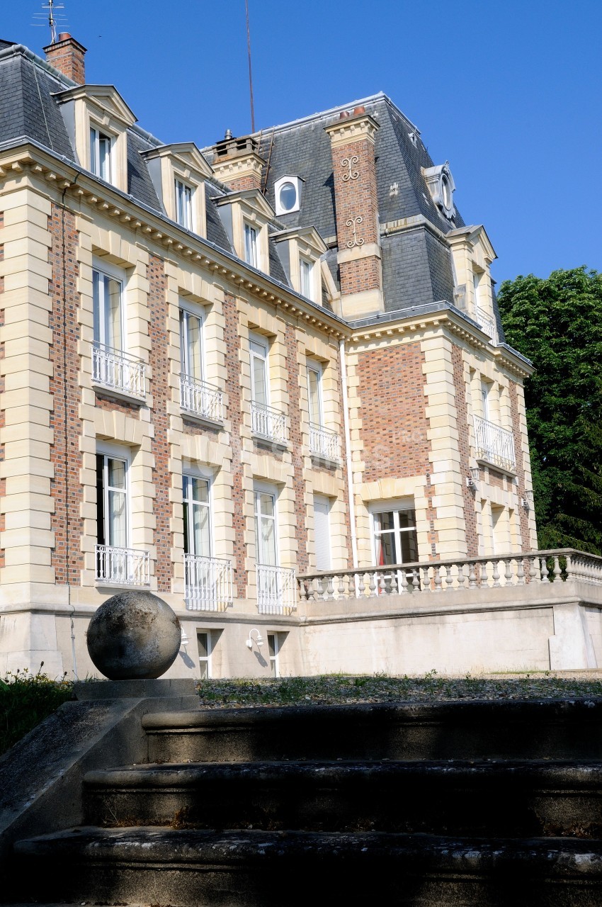 Façade d'un bâtiment ancien en briques et pierre, avec balcons et toit mansardé, entouré de verdure.