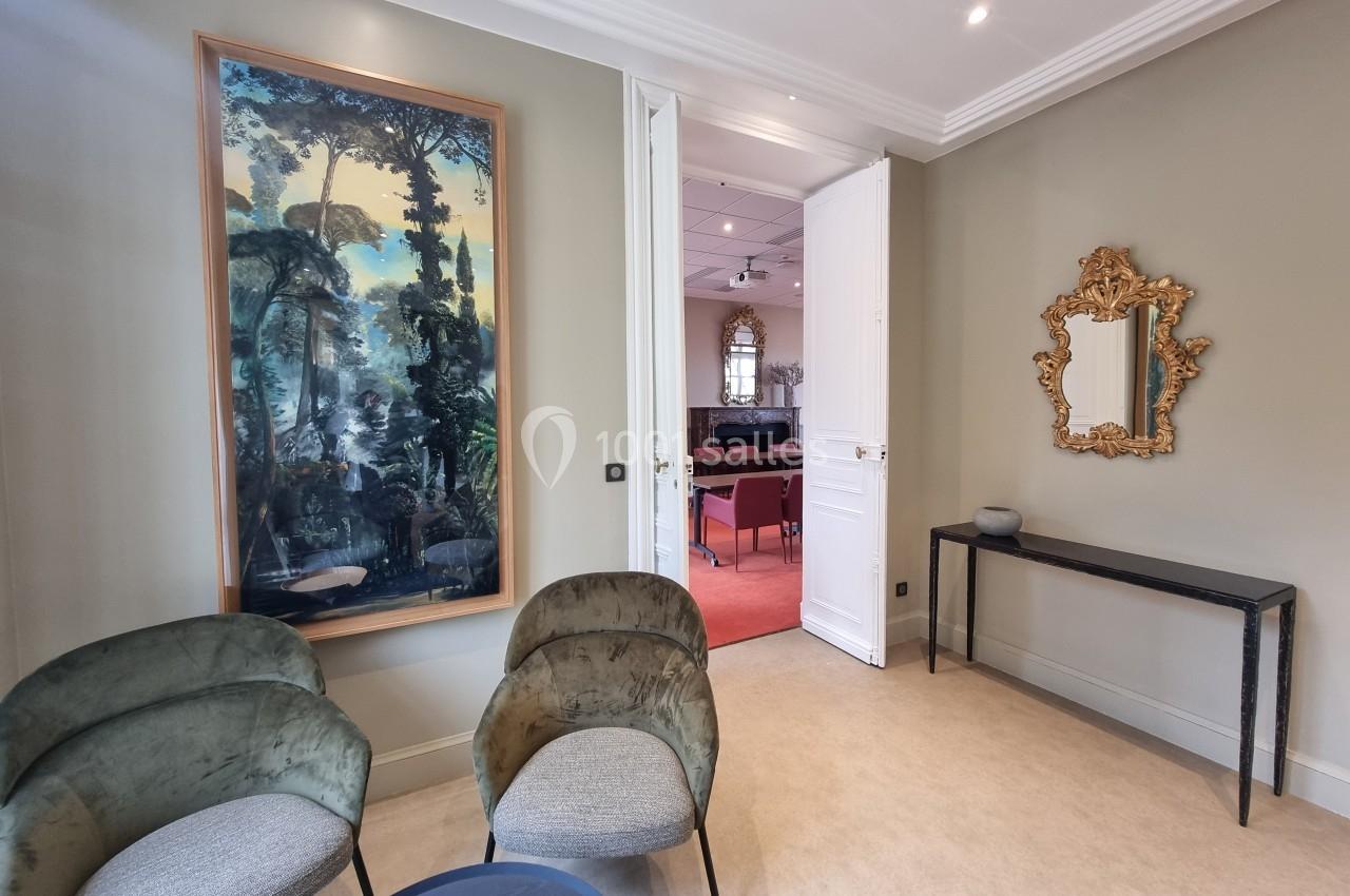 Deux fauteuils verts et une table basse dans un salon avec un tableau, un miroir doré et une porte ouverte sur une autre…