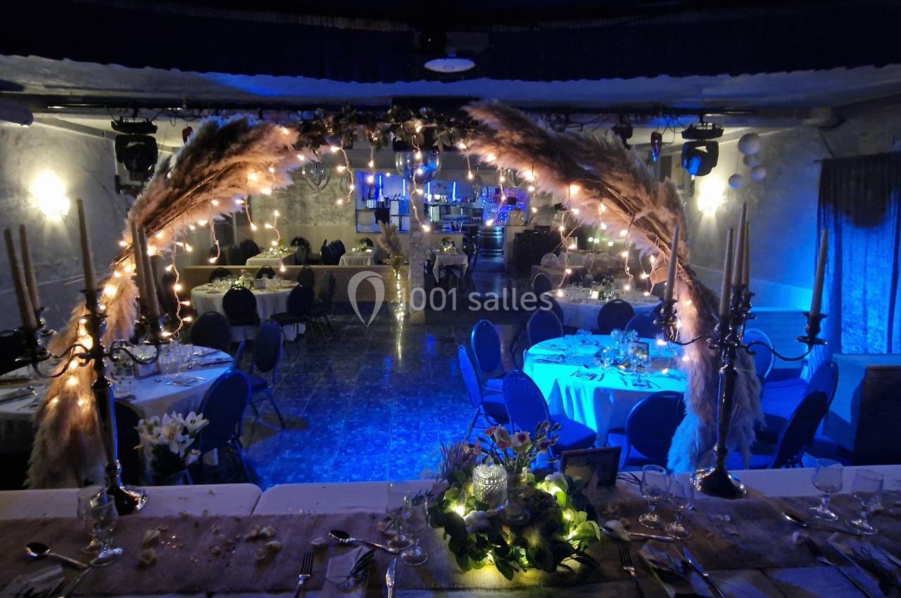 Salle de réception décorée avec des guirlandes lumineuses, des pampas et des tables dressées pour un événement.