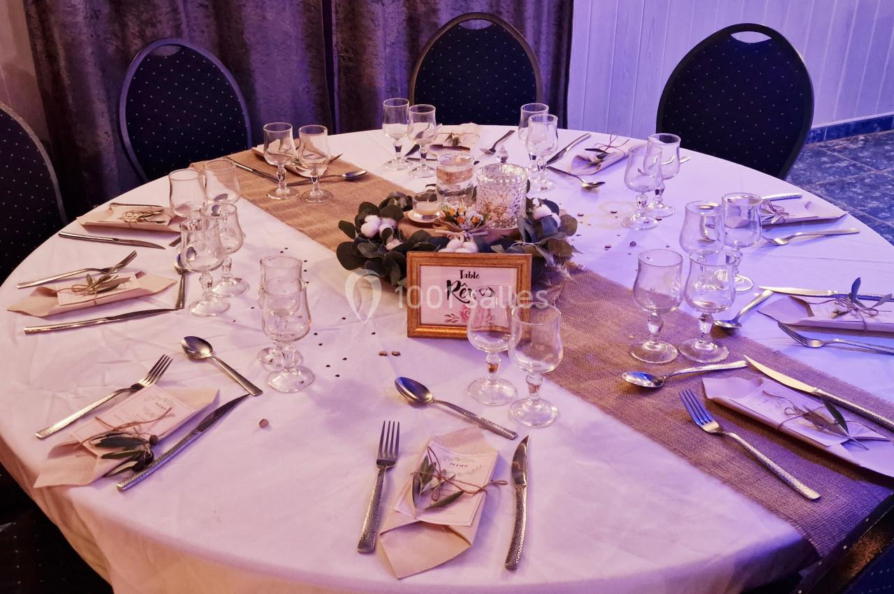 Table ronde élégamment dressée avec nappes blanches, couverts, verres, centre de table floral et pancarte ’Table Rêve’.