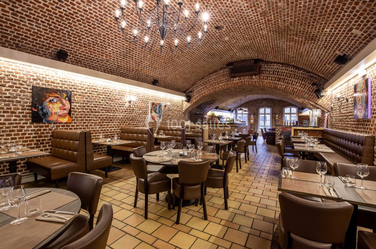 Salle de restaurant voûtée avec murs en briques, tables dressées et éclairage chaleureux.