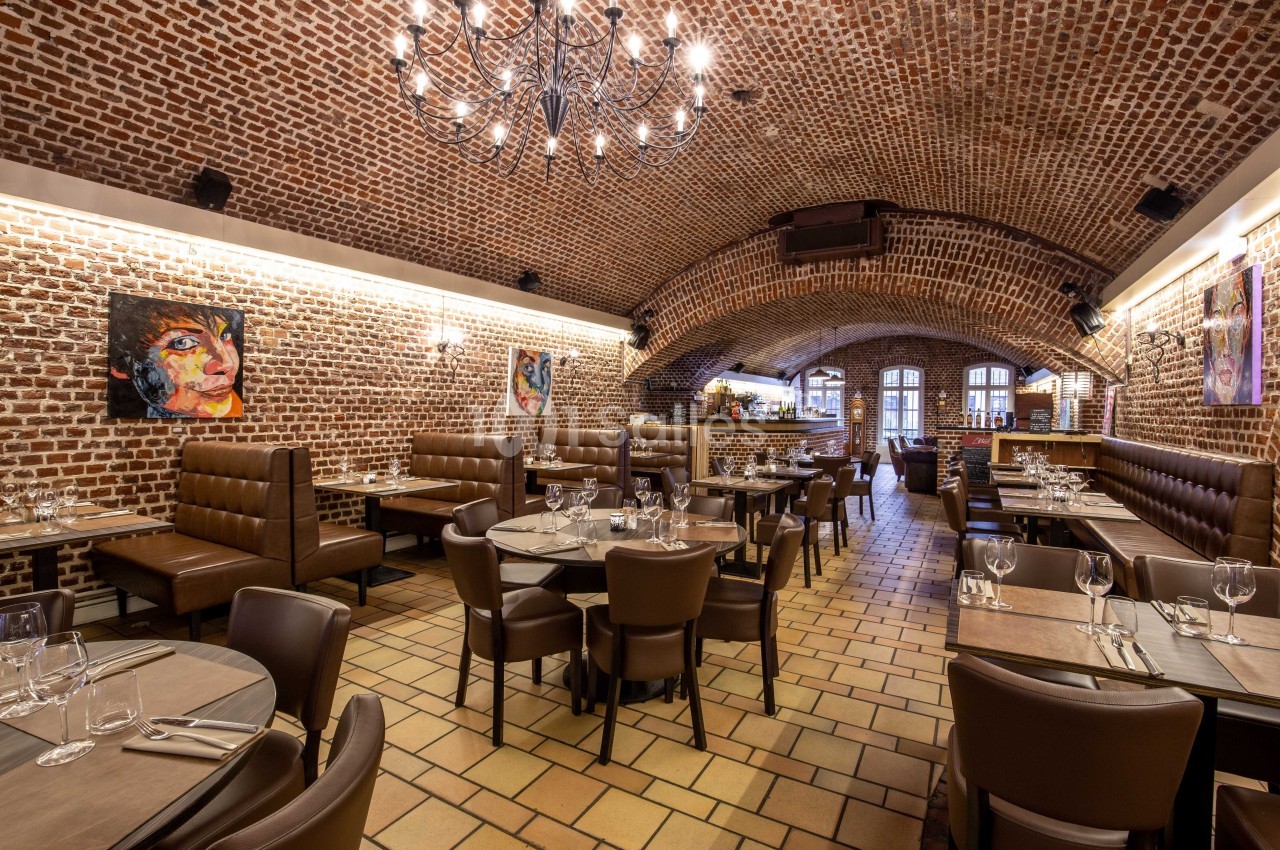 Salle de restaurant voûtée avec murs en briques, tables dressées et éclairage chaleureux.