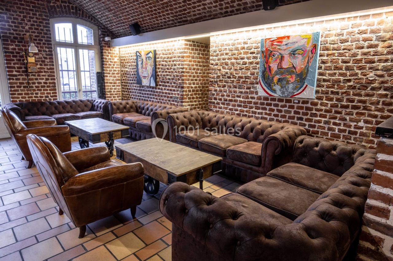 Salon avec canapés en cuir marron, tables basses en bois et murs en briques ornés de portraits colorés.