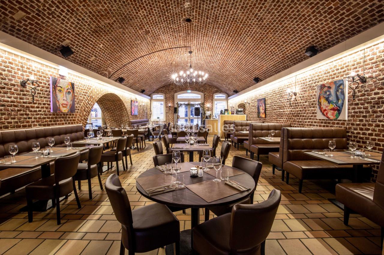 Salle de restaurant avec voûtes en briques, tables dressées et peintures colorées accrochées aux murs.