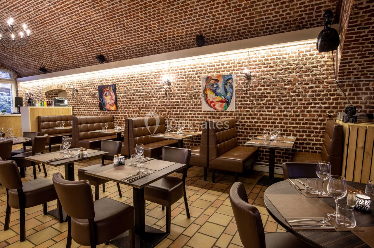 Salle de restaurant avec murs en briques, tables dressées, banquettes en cuir et tableaux colorés accrochés au mur.