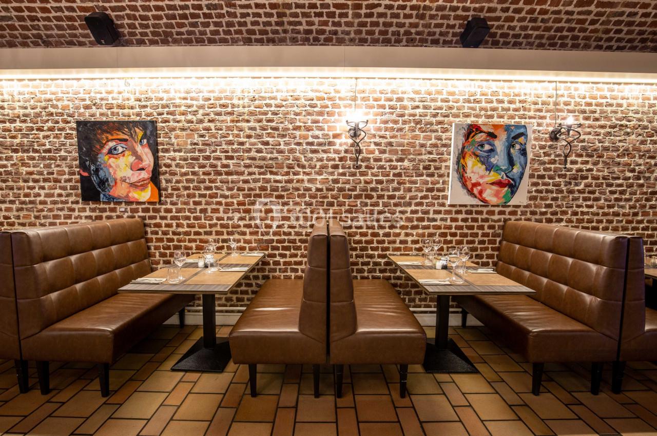 Banquettes en cuir marron dans un restaurant avec murs en briques, tableaux colorés et tables dressées.