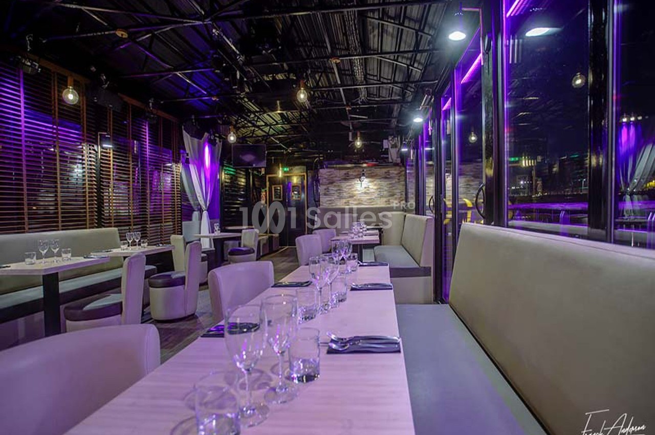 Salle de restaurant moderne avec tables dressées, éclairage violet et grandes baies vitrées.