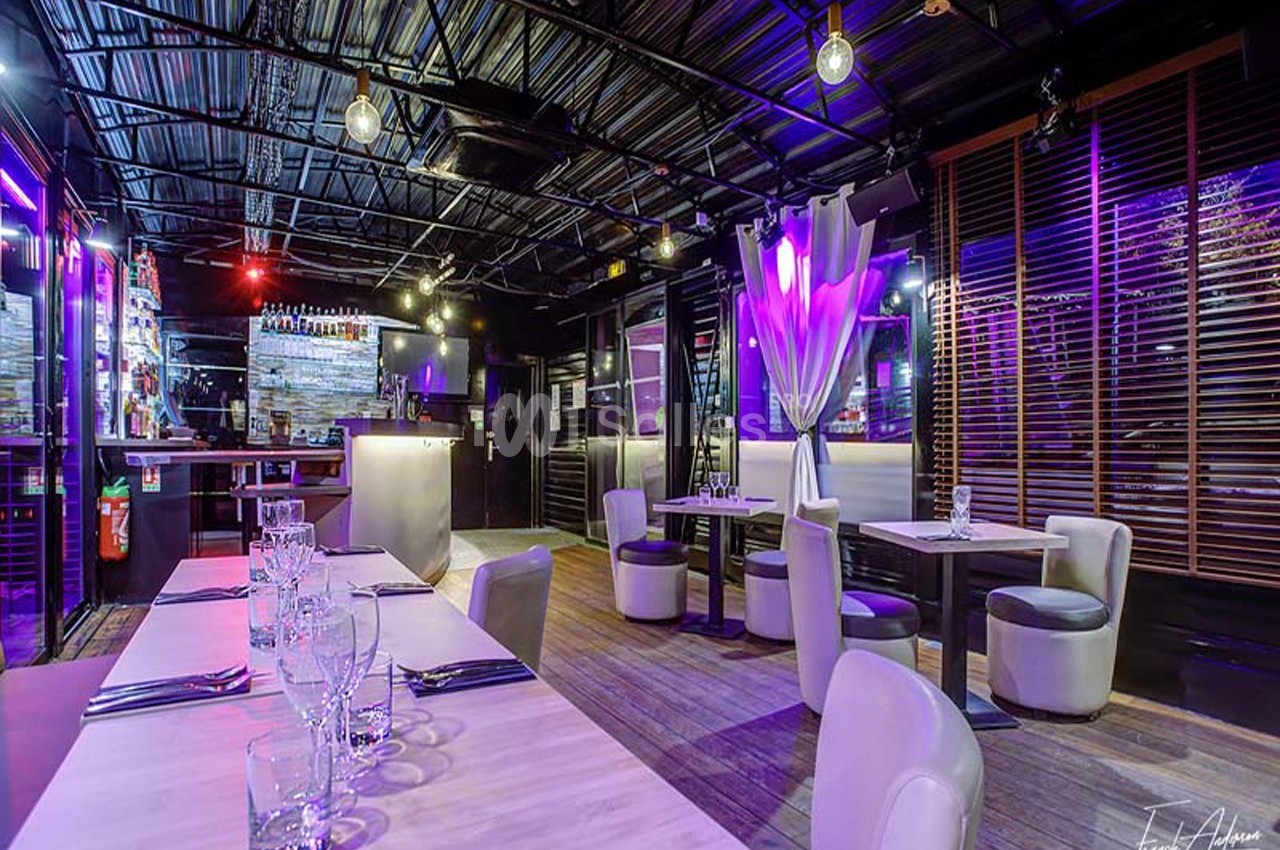Salle de restaurant moderne avec éclairage coloré, tables dressées et ambiance tamisée.