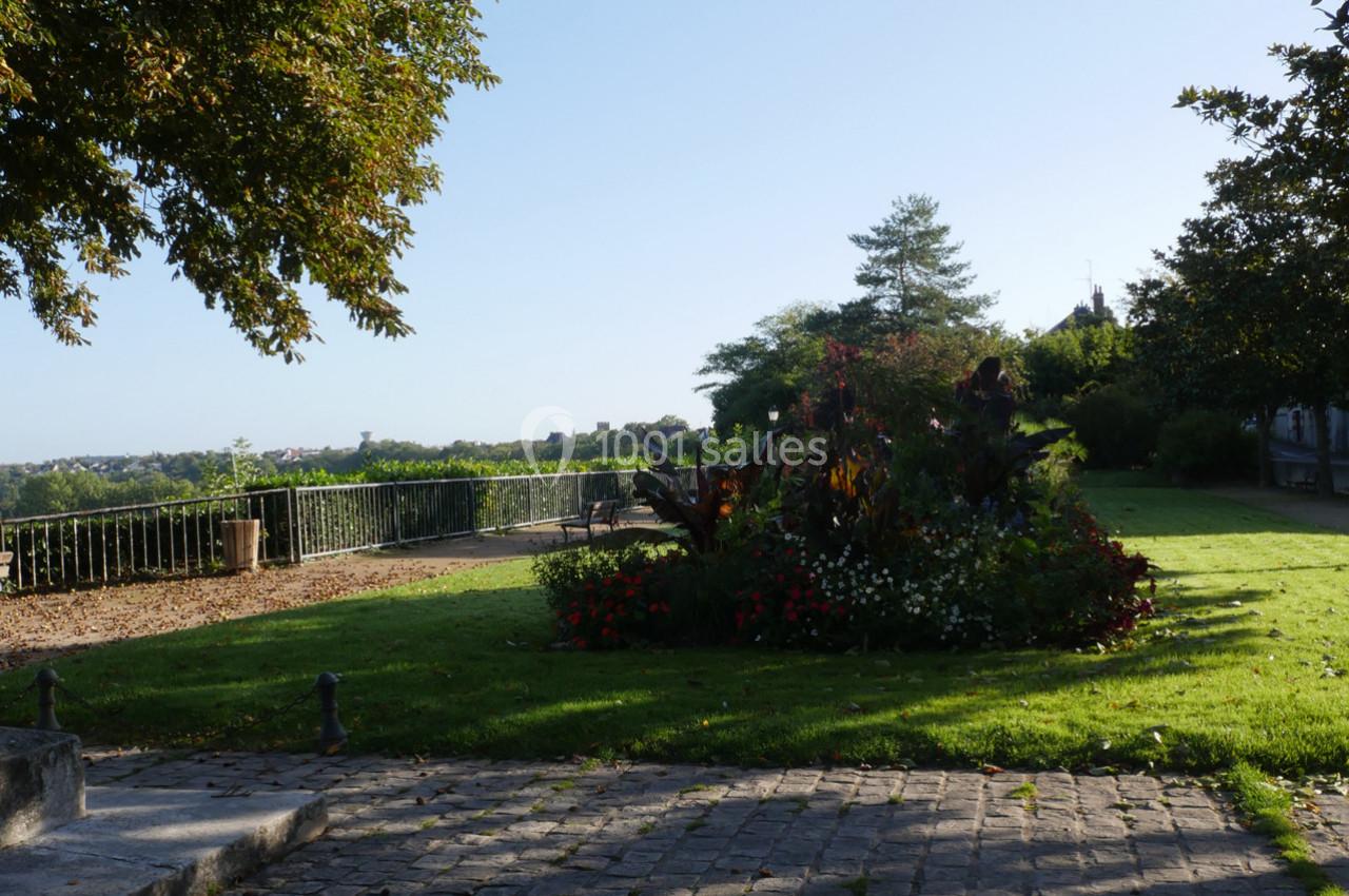 Jardin avec parterre fleuri, pelouse et vue dégagée sur un paysage lointain sous un ciel clair.