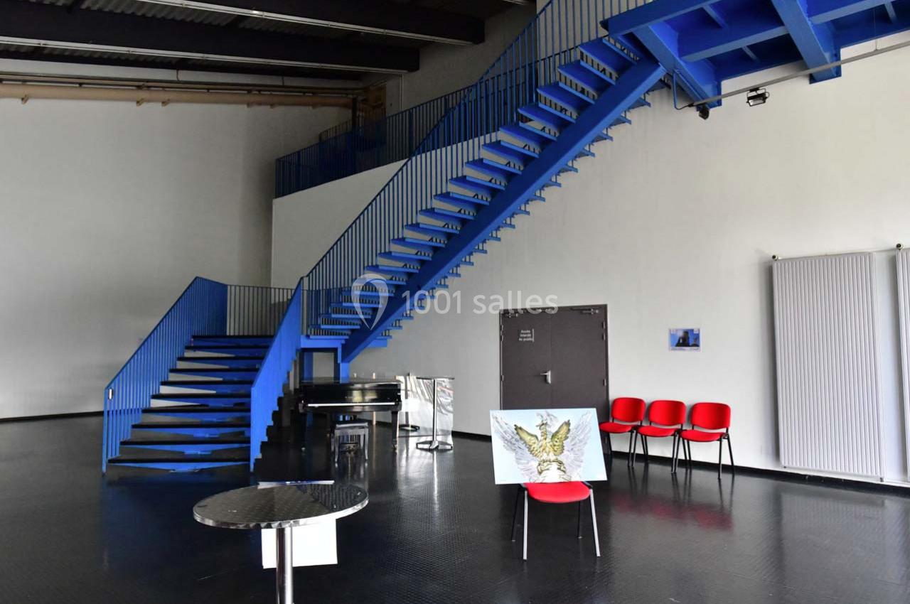 Escalier bleu métallique dans un espace intérieur moderne avec des chaises rouges et une peinture exposée.