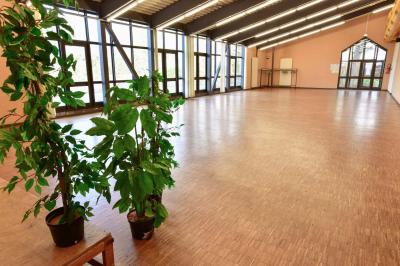 Salle spacieuse avec parquet en bois, grandes baies vitrées et quelques plantes en arrière-plan.