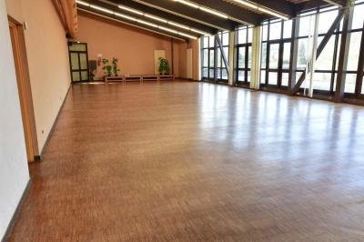 Salle spacieuse avec parquet en bois, grandes baies vitrées et quelques plantes en arrière-plan.