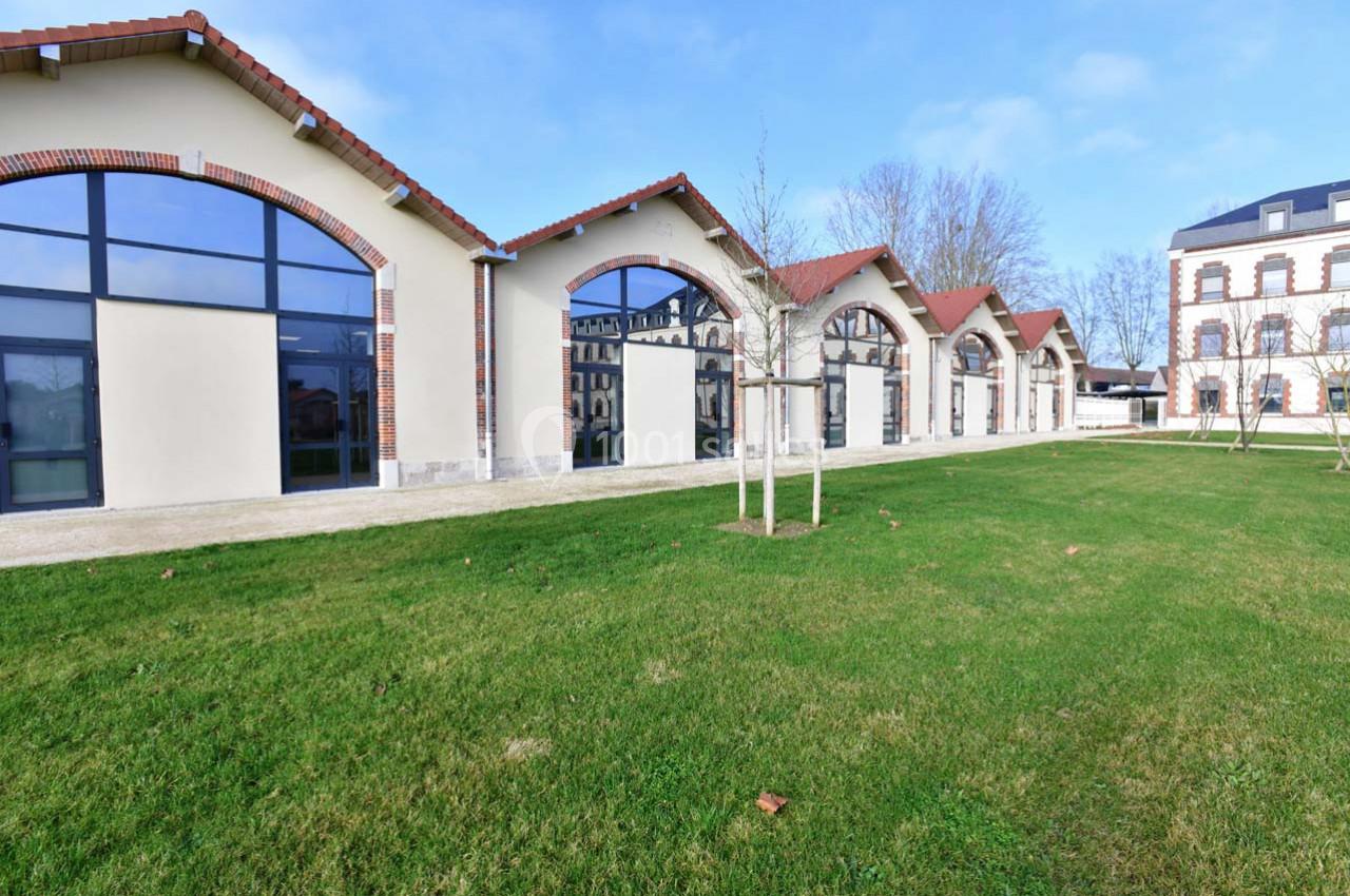Bâtiments rénovés avec grandes baies vitrées en arc, entourés d'une pelouse et d'arbres, sous un ciel dégagé.