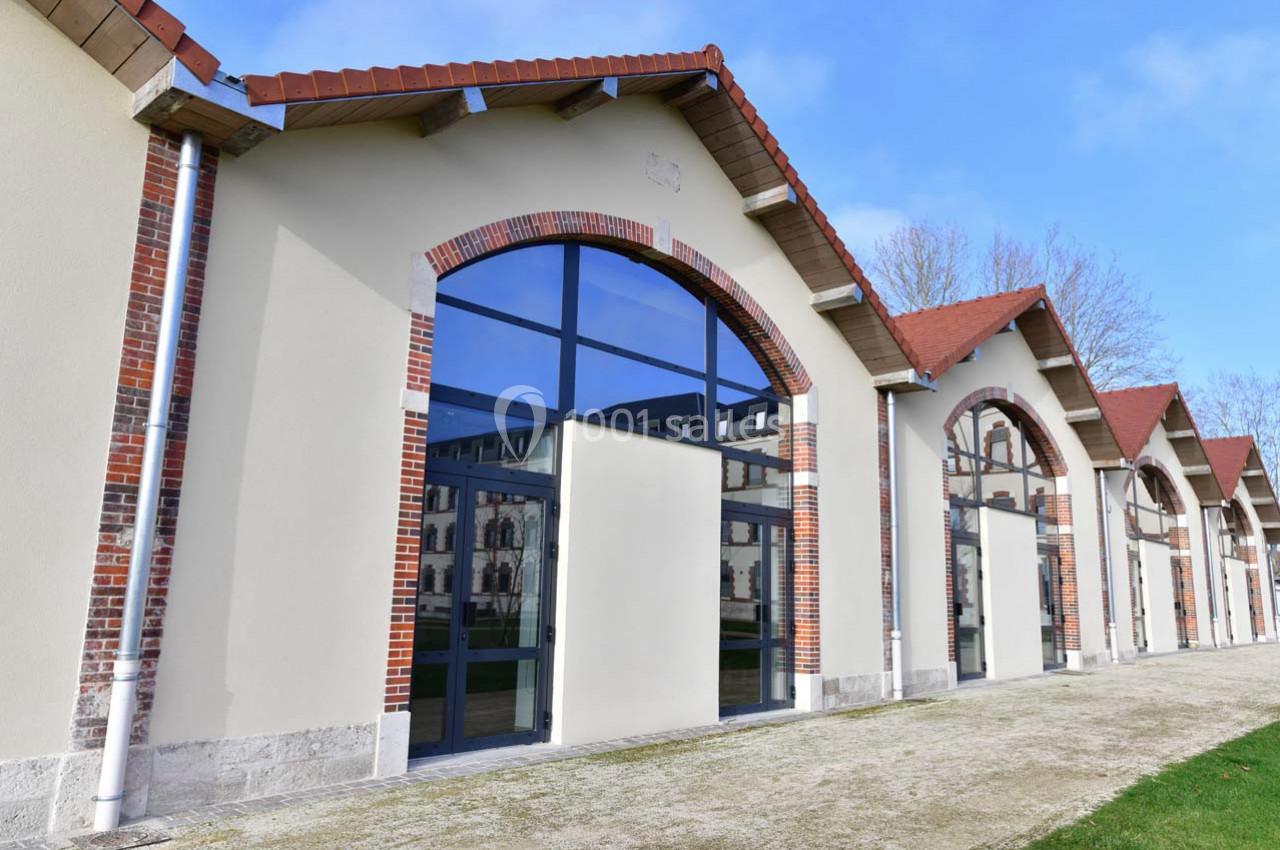 Façade d'un bâtiment rénové avec de grandes arches vitrées et des murs en briques et crépi beige.