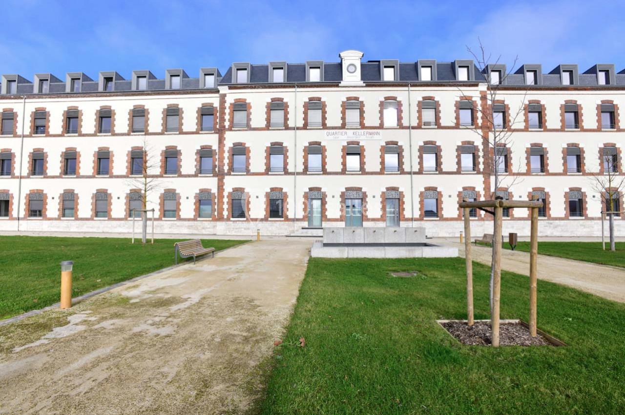 Façade d'un bâtiment rénové à trois étages avec des fenêtres alignées, entouré d'une pelouse et de chemins.