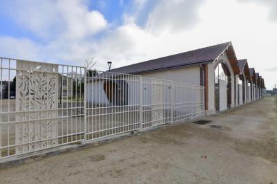 Bâtiment avec toit en tuiles et arcades, entouré d'une clôture métallique ornée de motifs végétaux.