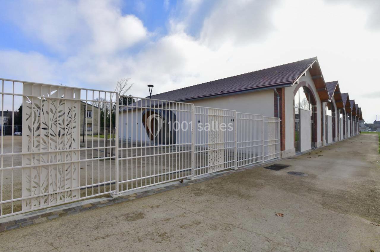 Bâtiment avec toit en tuiles et arcades, entouré d'une clôture métallique ornée de motifs végétaux.