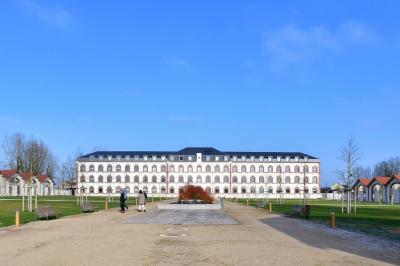 Bâtiment avec toit en tuiles et arcades, entouré d'une clôture métallique ornée de motifs végétaux.