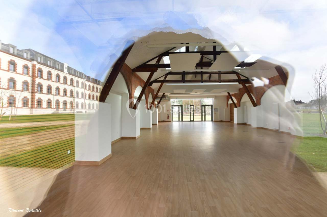 Salle lumineuse avec parquet clair, poutres apparentes et grandes baies vitrées donnant sur un espace extérieur verdoyant.