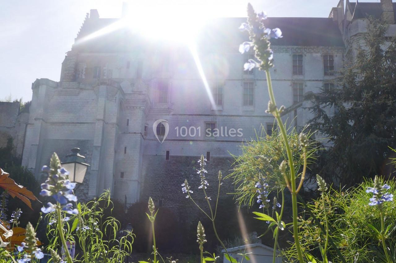 Vue en contre-plongée d'un bâtiment ancien en pierre, éclairé par le soleil, avec des fleurs au premier plan.