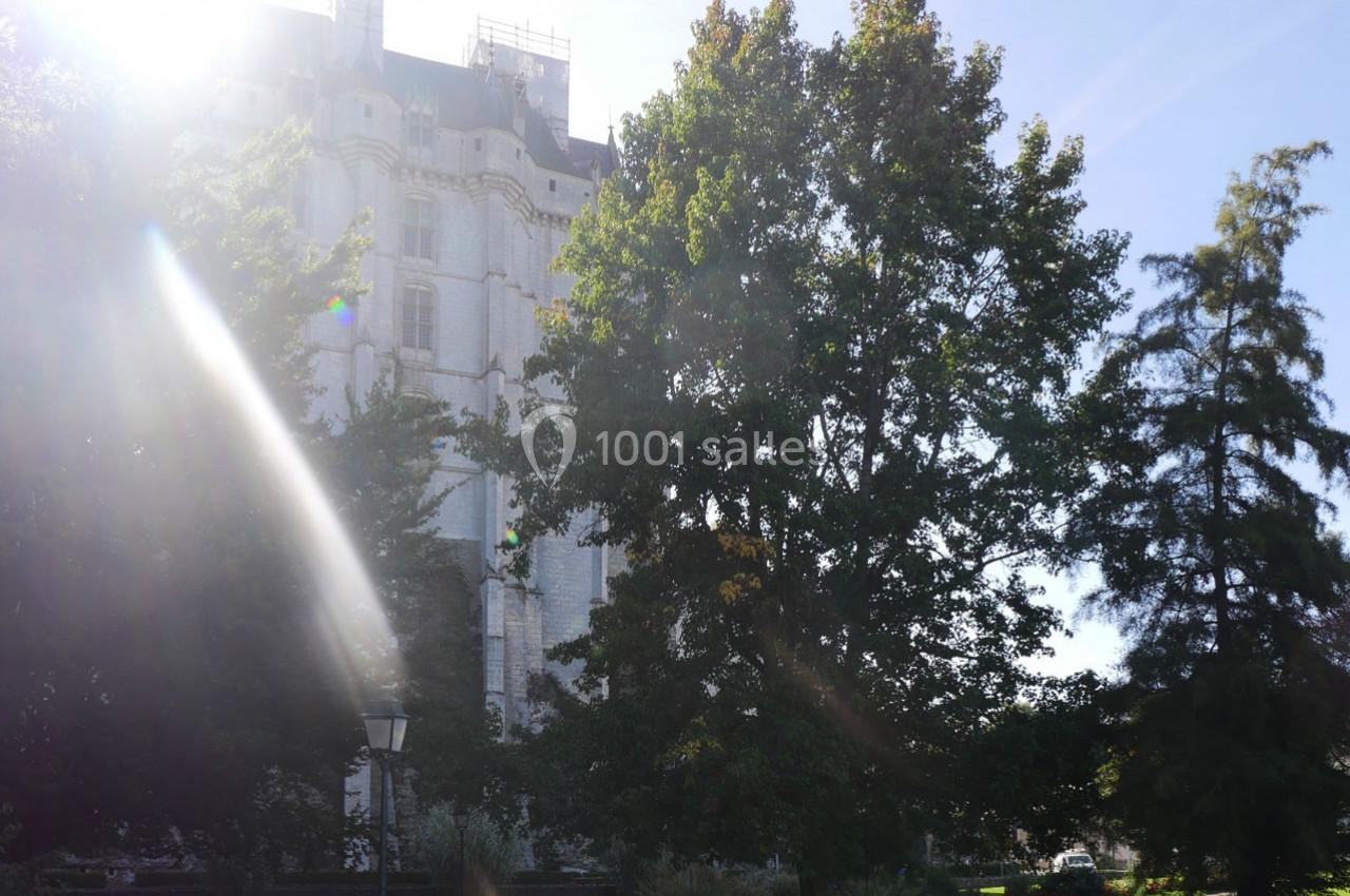 Façade d'un bâtiment historique en pierre partiellement cachée par des arbres sous un ciel ensoleillé.
