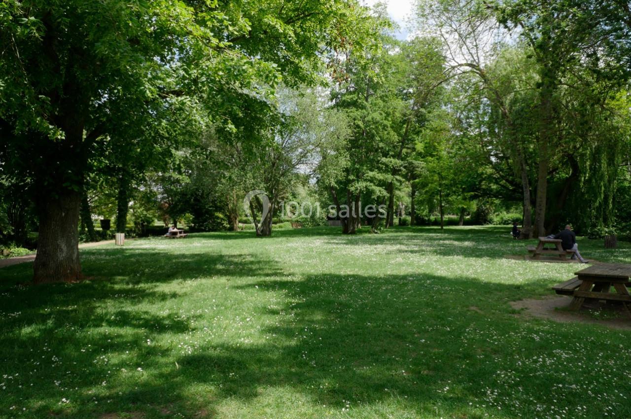 Un parc verdoyant avec des arbres, une pelouse parsemée de petites fleurs blanches et des tables de pique-nique.